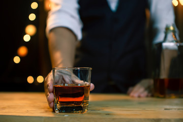 The bartender poured a glass of whiskey on wood bar counter.