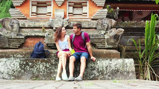 Sweet young couple in love have a conversation sitting on stone stairs of ancient Buddhist temple in Bali, travel concept