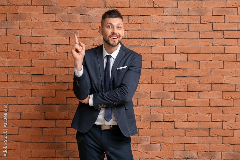 Wall mural Businessman with raised index finger on brick background. Concept of choice