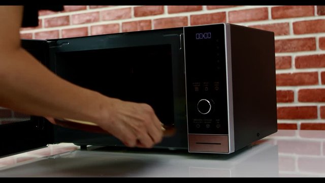 Close up scene video of chef put a pizza into a microwave oven to bake a delicious dish.