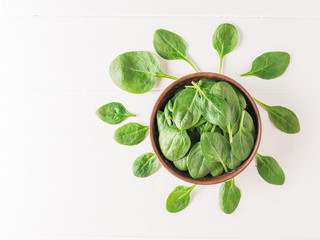 Fresh spinach leaves with a clay bowl on a white wooden table. Food for fitness. The view from the top.