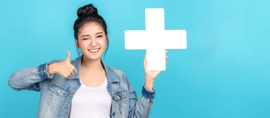 Fotobehang Banner of asian woman smiling, showing plus or add sign and thumb up on blue background. Cute asia girl wearing casual jeans shirt and showing join sign for increse and more benefit concept © ChayTee
