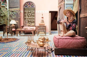 Foto op Canvas Reizen door Marokko. Gelukkig jonge vrouw in hoed ontspannen in traditionele riad interieur in medina. © luengo_ua