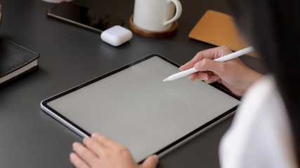 Cropped shot of a woman drawing on mock up tablet on black table background