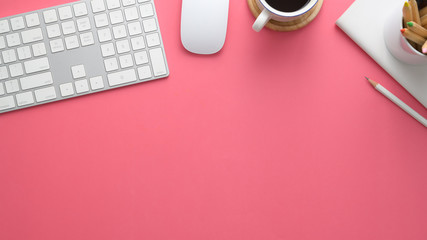 Overhead shot of stylish workspace with computer, stationery, coffee cup and copy space on pink table