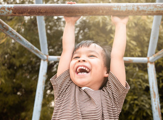 Fototapeta premium Cute Asian little girl hanging the monkey bars by her hand to exercise at out door playground on sunny day.