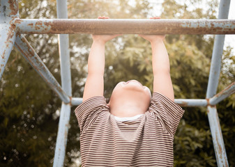 Fototapeta premium Cute Asian little girl hanging the monkey bars by her hand to exercise at out door playground on sunny day.