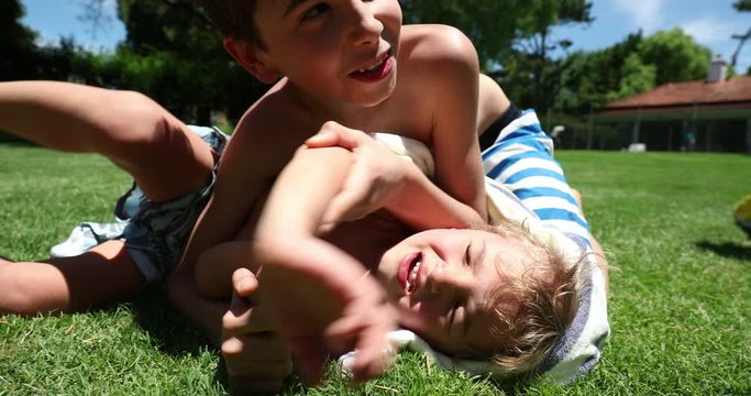 Brother wrestling younger toddler outside in backyard home. Siblings quarrel conflict outdoors