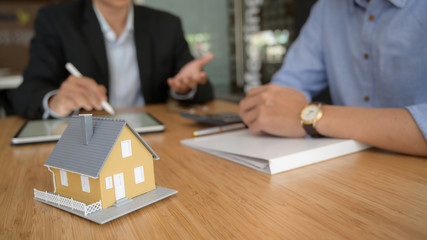 Close up view of real estate agent using  blank screen tablet with house model on wooden desk