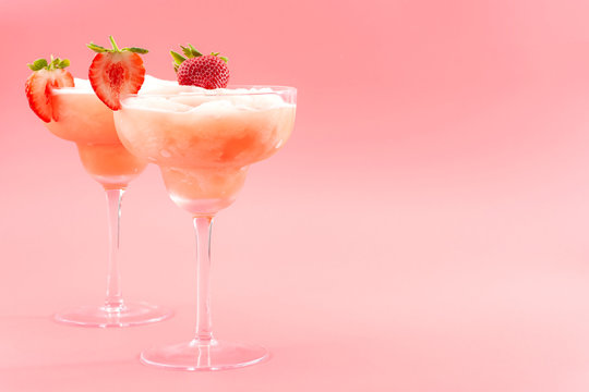 Mixed cocktails, party punch smoothies and frozen summer drinks concept with strawberry mojito or daiquiri in margarita glasses and fruits used as garnish isolated on pink background with copy space