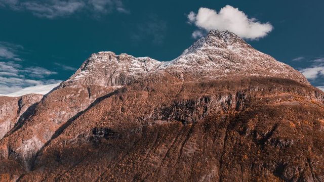 Magnificent mountain towering above still waters of the fjord. White wispy clouds whirling above. Fresh snow on the mountain tops. Aerial view.