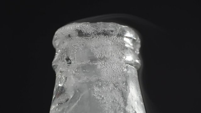 Close-up shot of opening the bottle with iced sparkling drink. Cool freshness. Isolation on black