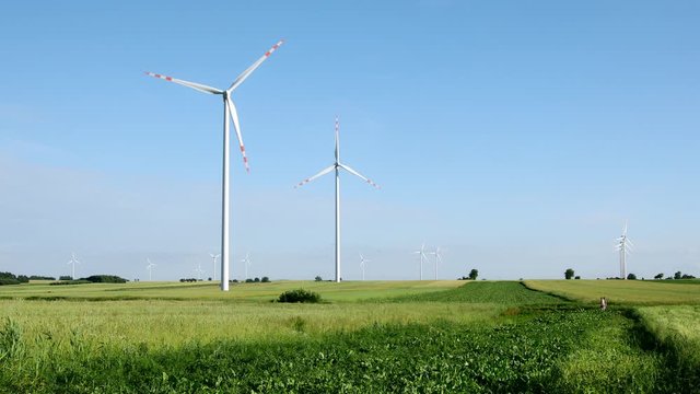 white wind turbines in bright blue sky in countryside meadow, 4k