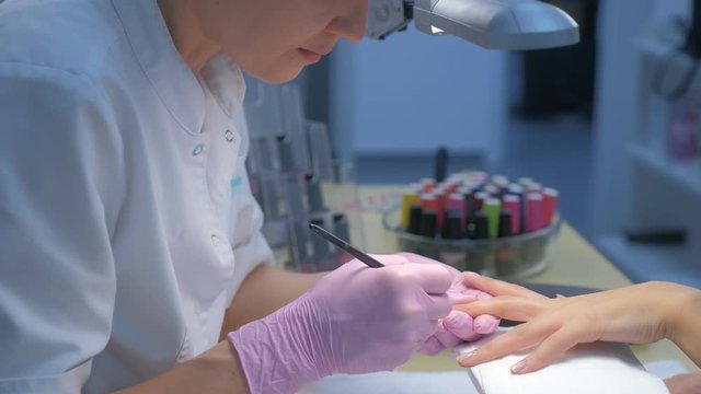 Manicurist master is painting nails for client woman gel shellac using brush in beauty salon clinic, side view. Portrait of manicurist woman working making manicure.