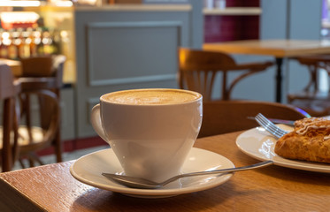 A cup with cappuccino and cookies on a plate on a table with a wooden surface. Breakfast at the cafe. Coffee break.