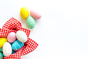 Easter eggs painted in basket on white desk top-down copy space