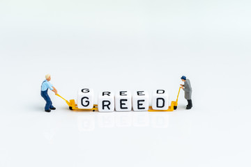 Miniature man pulling folklift with cube block building the word GREED on clean white background using as greed and fear in stock market or money game and financial investment