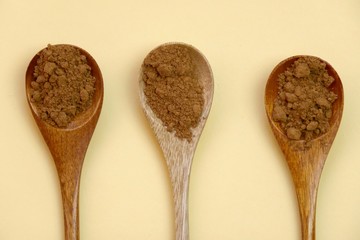 guarana powder in wooden spoons set  on a light yellow background.Portion of Guarana Powder 