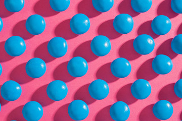 Blue round chocolate candies on a pink background with a tight shadow