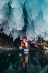 Baikal, Russia, March. A girl in winter clothes lies on ice in an ice cave. Smile. Around the icicles hanging very karis and unusual shape.