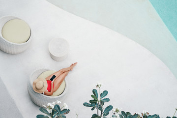 Enjoying suntan. Vacation concept. Top view of young woman on the sun lounger near  the swimming pool in tropical garden..