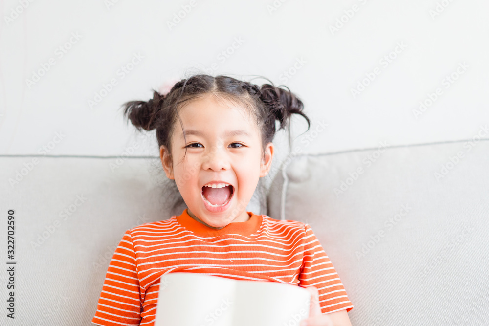 Wall mural Little asian girl Happy smiley excited face and open red gift box in heart shape in sofa at home on white wall background.Child girl holding gift box in Valentine day, Christmas and New year concept.