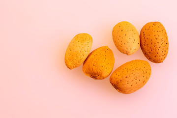 five unpeeled almonds on a light pink background. about the benefits of nuts when losing weight