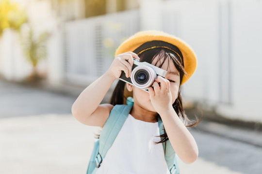 Cute Little Asian Girl Takes Picture With Camera For Mom.Traveller Cheerful Toddler Girl Holding Mirrorless Camera.Vacation Travel Lifestyle, Education And Smart Kid Girl Concept.