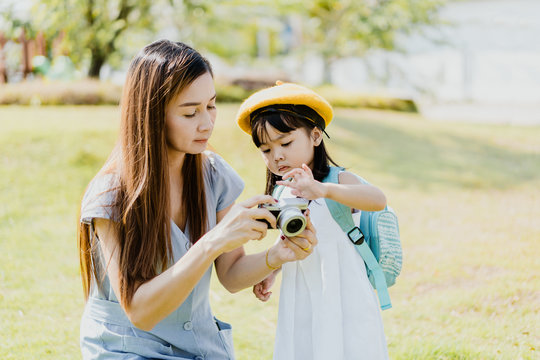 Asian thai mother and toddler child baby girl holding retro vintage photo camera in green park.Mother and daughter in playground.Little asian kid daughter. Mother's Day, Parenting family concept.