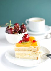 Slice of cake with fruits and cherry on top. Homemade tasty youghurt and fruit cake served with cup of tea.