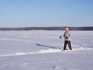 Elderly woman doing Nordic walking in winter sunny day on a snow-covered lake, outdoor.