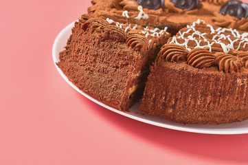 Cuted chocolate cake on white round plate on pink background. Copy space