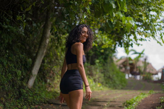 natural lifestyle portrait of young attractive and happy hipster woman with curly hair in fitness clothes enjoying nature outdoors smiling cheerful exploring rural road