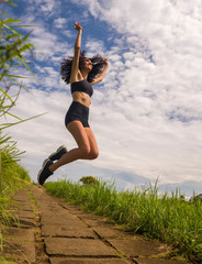 natural lifestyle portrait of young attractive and happy hipster woman with curly hair feeling free jumping on the air enjoying nature outdoors smiling cheerful and carefree