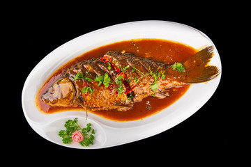 whole baked fish in spicy Chinese sauce on a black isolated background