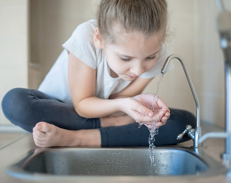 Caucasian little girl drinking fresh water in kitchen at home. Thirsty baby. Hands open for drinking tap water. Healthy Eating and Drink. Environment and health care concept. World Water Day
