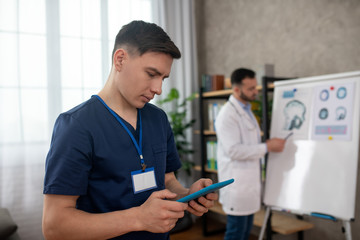 Obraz premium Dark-haired young doctor typing a message on a tablet