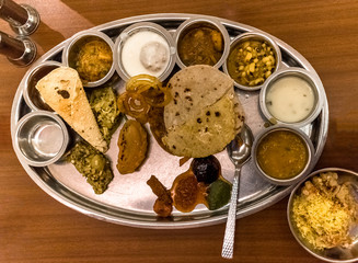 Food plate - full of Indian Cuisine, consisting variety of traditional dishes from all over India on a wooden table in background. An Indian Delicacy, it is healthy, spicy and epicure treat 