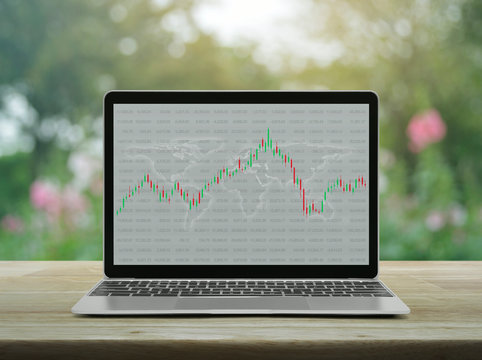 Trading graph of stock market with world map and graph on modern laptop computer on wooden table over blur pink flower and tree in garden, Business investment online concept, Elements of this image fu