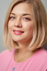 Portrait of happy blonde woman smiling and looking at camera on grey background.