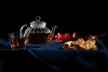 Hot tea in a glass teapot on a black background. saucer with cookies