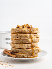 Oatmeal banana pancakes with cinnamon, chopped walnuts and maple syrup. Healthy morning breakfast, white wooden background, close up view, copy space.