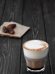 Glass cup of coffee with milk on a dark wooden background. Hot latte or cappuccino prepared with milk on a rustic wooden table with copy space. Near dates fruits.