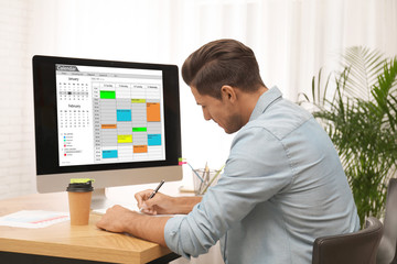Handsome man planning his schedule with calendar app on computer in office