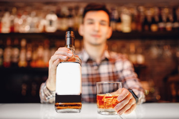 Barman holds out glass of whiskey with ice to male visitor. Concept rest in bar