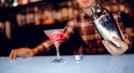 Barman is preparing mix cocktail in shaker of red alcohol and ice glass, bar counter