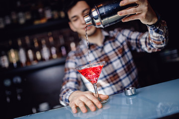 Barman is preparing mix cocktail in shaker of red alcohol and ice glass, bar counter