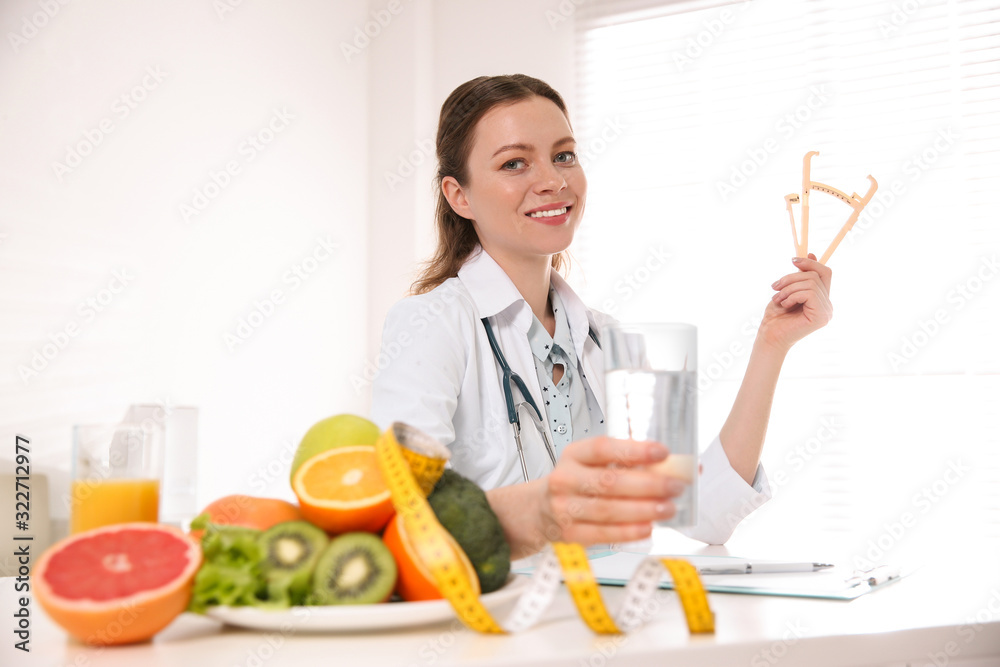 Wall mural Nutritionist with caliper and glass of water at desk in office