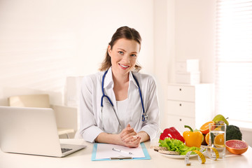 Nutritionist with clipboard and laptop at desk in office