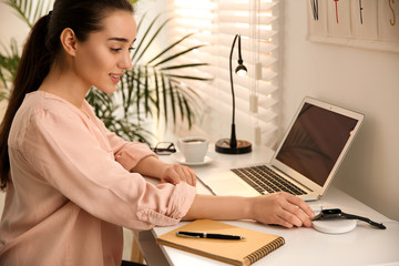 Woman putting smartwatch onto wireless charger at white table. Modern workplace accessory